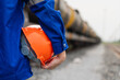 © Nattawit - A worker in blue coverall uniform is holding an orange safety hardhat or protective helmet, standing in front of crude oil train tanker. Ready to work in challenge industrial scene, close-up.