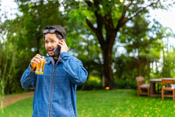 Wall Mural - Happy Asian man speaking on mobile phone during having dinner with friends. People enjoy celebration reunion meeting outdoor party with food and drink in the garden at restaurant on holiday vacation.