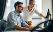 © StockLab - Middle age man in blue shirt working and explaining a computer screen to his female older senior colleague or a manager
