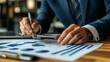 © fotofabrika - A business professional analyzes financial reports while writing notes in a modern office setting during daytime