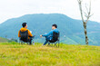 © CandyRetriever  - Two Asian man friends sitting on outdoor chair and drinking coffee together during camping on the mountain. People enjoy outdoor lifestyle travel nature hiking at forest mountain on holiday vacation.
