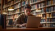 © Aliaksandr Siamko - Young man using a laptop with a blank screen at a desk in a library setting for a mockup of an e-learning site