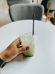 Hand holding cup of matcha green tea latte in a cafe restaurant or coffee shop