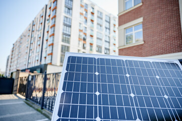 Photovoltaic solar panel in front of modern apartment building with balconies, suggesting residential or mixed-use. Concept of integration of sustainable renewable energy sources into architecture.