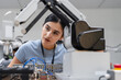 © Nassorn - Hispanic engineer woman working on AI technology in robotics electronics engineering laboratory. University students' research project is programming robot machine with intelligent mechanical control
