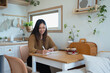 © Prathankarnpap - Pleased young woman sitting at kitchen table and writing in a notebook