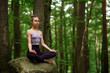 © fesenko - Cute woman doing yoga outdoors in the forest, sitting on a big stone in the lotus position