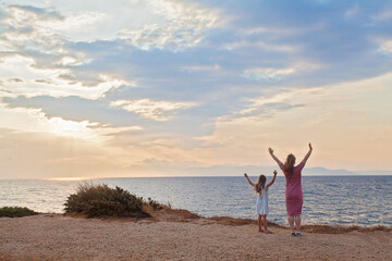 Mother and her daughter enjoying walk along beach at sunset. The woman and child having fun