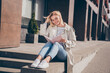 © deagreez - Full body photo of pretty young blonde woman reading book sit concrete border wear stylish trench coat walk outside urban city streets