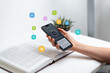 © Stanisic Vladimir - Hand holding smartphone above open book, using voice-to-text app for learning, representing audio search and text-to-speech technology, with floating icons for study and communication concepts