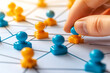 © L.S. - Close-up of a hand placing blue and yellow pawn pieces on a connected network diagram, symbolizing strategic planning, teamwork, and social connections