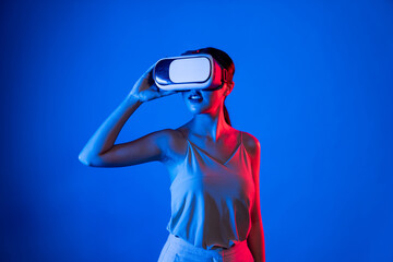 Sticker - Smart female standing hit by neon light wearing VR headset connecting metaverse, futuristic cyberspace community technology. Elegant woman confidently pose while look into virtual area. Hallucination.