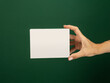 © Pedro - Close-up of a hand holding a blank white card against a green background. Perfect for mockup designs, presentations, or advertising concepts, offering ample space for customization