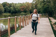 © mdyn - A happy woman hiker with a green backpack smiling and hiking near lake. Tourism and travel, Lifestyle adventure concept. 30s girl enjoying of nature. Full body