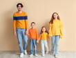 © Pixel-Shot - Happy family in warm sweaters holding hands near beige wall