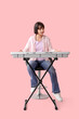 © Pixel-Shot - Young woman playing synthesizer on pink background