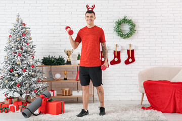 Sticker - Young happy man training with dumbbells in living room decorated for Christmas