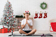 © Pixel-Shot - Young man in reindeer horns practicing in yoga in living room decorated for Christmas