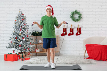 Sticker - Young happy man in Santa hat training with skipping rope in living room decorated for Christmas