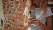 © Vii - A woman stands next to a brick wall, focused on her cell phone