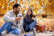 © Mediteraneo - Young happy couple having picnic in a grass in a colorful autumn park. They drink coffee from thermos.