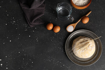 Canvas Print - Plate with fresh raw dough, wheat, eggs, sugar and bowl of flour on black background