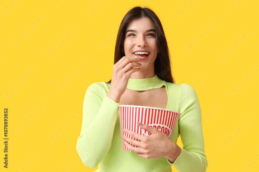 Young happy woman eating popcorn on yellow background