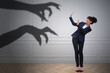 © New Africa - Businesswoman scared by hands of monster reaching for her. Creepy shadow on white wall