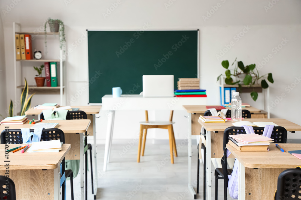 Interior of light classroom with blackboard, desks and backpacks