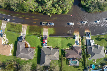 Flooded american street with moving vehicles and surrounded with water houses in Florida residential area. Consequences of hurricane natural disaster