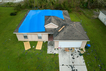 Top view of leaking house roof covered with protective tarp sheets against rain water leaks until replacement of asphalt shingles. Damage of building rooftop as aftermath of hurricane Ian in Florida