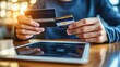 © setiadio - A person holding credit cards and using a tablet for online transactions.