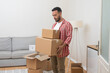 © olga_demina - Young man, Caucasian, moves into his new home, standing in the living room with a heap of cardboard relocation boxes, marking the transition