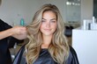 © zakiroff - A hairstylist adds finishing touches to a smiling woman with long, wavy, blonde hair in a modern salon during daytime