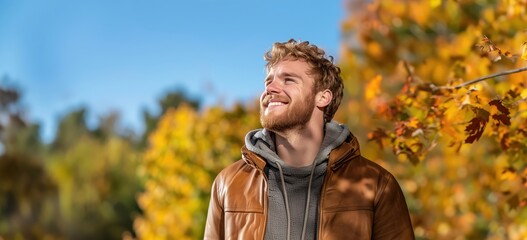 Wall Mural - Smiling young man outdoors in a autumn landscape, wearing a warm jacket, enjoying the bright sunlight and crisp air, conveying happiness.