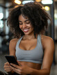 © The Stock Photo Girl - A smiling woman in athletic wear checks her phone in a gym setting.