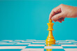 © carolina - Hand moving a yellow chess piece on a chessboard with a blue background, showcasing strategy and competition in chess banner/web/design/poster