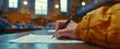 © Witri - A student's hand writes on a paper in a large lecture hall, the focus is on the hand and the paper.