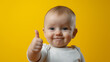 © Tatiana Sdvyzer - Happy baby giving thumbs up, expressing positivity and joy against a vibrant yellow background