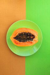 Poster - Half of a papaya on a green plate on a green-orange background