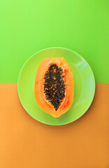 Poster - Half of a papaya on a green plate on a green-orange background