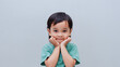 © arthierry - Studio portrait of a adorable little boy holding his cheeks with his hands on a grey background