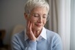 © hobonski - A peaceful, contemplative senior woman with short, gray hair and glasses gently touches her face. She is dressed in a soft blue sweater and exudes a sense of calm and tranquility.