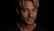 © Gavasol - Young man with stylish blonde hair displaying confidence and charisma against a dark background