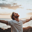 © Chanyapat - Man with arms stretched out, breathing easy and happy, enjoying sunset by ocean, feeling free and content in nature beauty