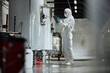 © Seventyfour - Full length shot of female process technician in hazmat suit using tablet computer inspecting stainless tanks while controlling fermentation process at craft cider factory, copy space