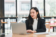 © PRIME STOCK LAB - young woman in black blazer smiles while working on laptop in modern office. She appears focused and engaged in her task