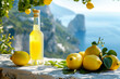 © alexandro900 - Una bottiglia di limoncello su un tavolo di pietra, circondato da limoni freschi, su una terrazza mediterranea con vista sui Faraglioni dell'isola di Capri, Italia
