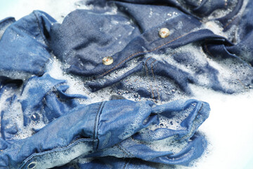 Many different denim clothes in basin with water and soap, closeup