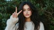 © Odin AI - A woman wearing a white sweater makes a peace sign with her fingers while standing amidst green bushes, exuding a playful and friendly aura.